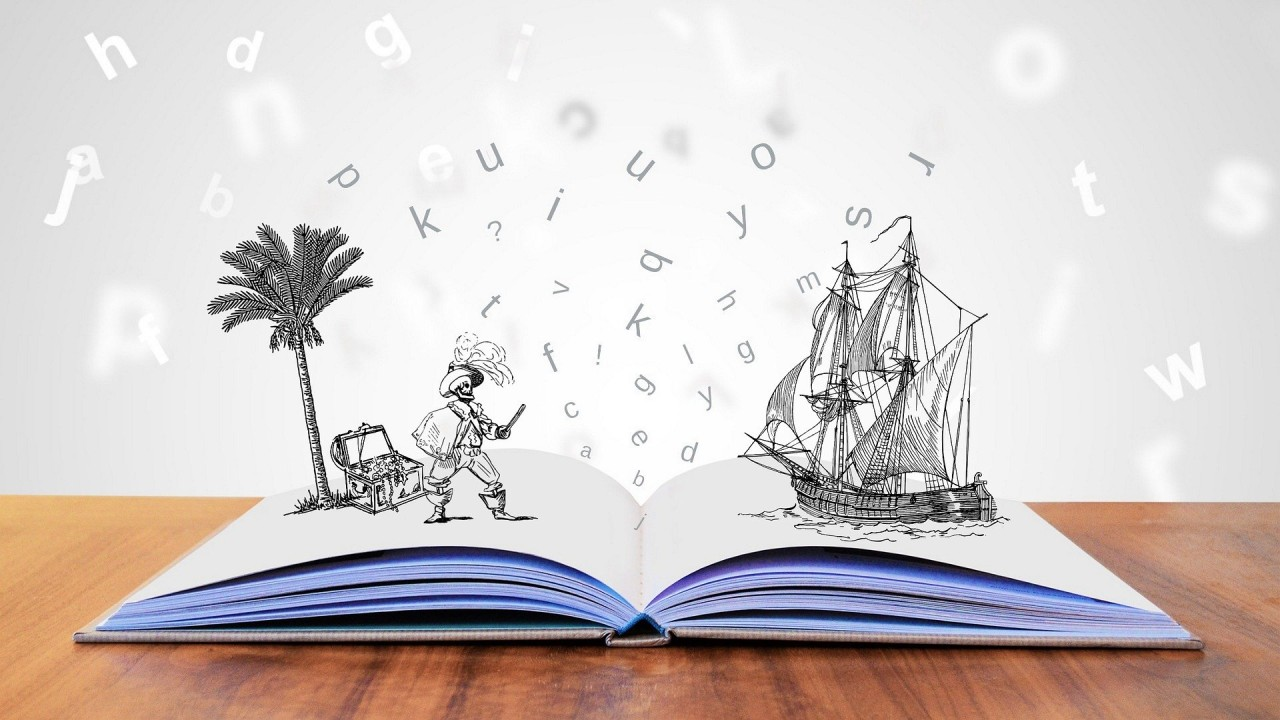 Livro aberto sobre uma mesa, com ilustrações de um navio, um pirata e uma palmeira saindo das páginas entre letras flutuando